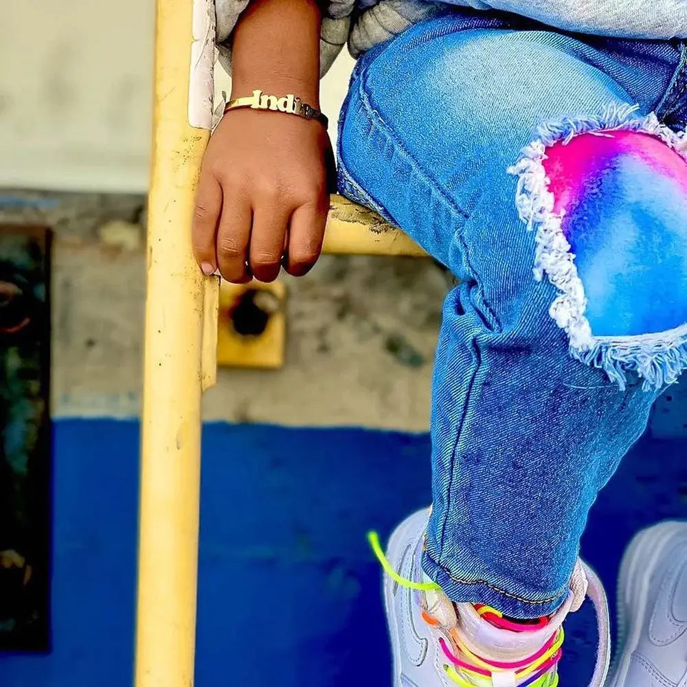Child’s ripped jeans with colorful knee patches beside a Personalised Stainless Steel Alphabet Bracelet