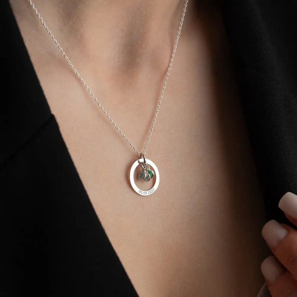 Silver necklace with circular pendant featuring green stone, a personalized engraved birthstone piece.